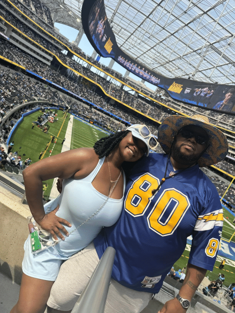 Couple at a football stadium, man wearing a straw lifeguard hat with printed under brim, highlighting custom design for events.
