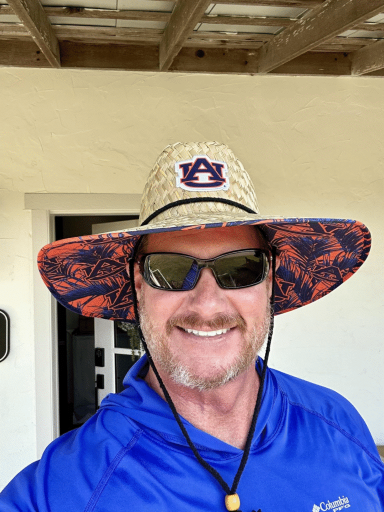 Man wearing a custom straw lifeguard hat with logo patch, smiling outdoors, promoting sun protection and branding.