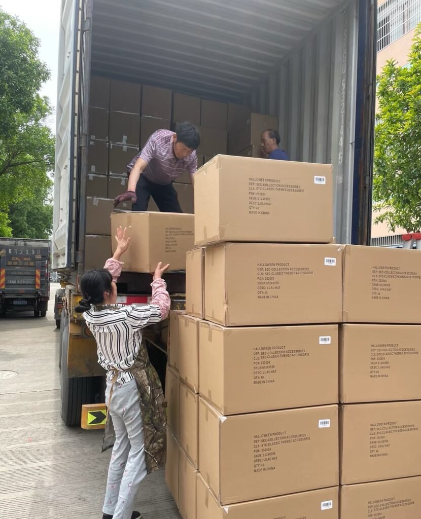 workers loading large boxes of Halloween-themed straw cowboy hats into a truck, demonstrating the shipping process of bulk hat orders in a factory setting.