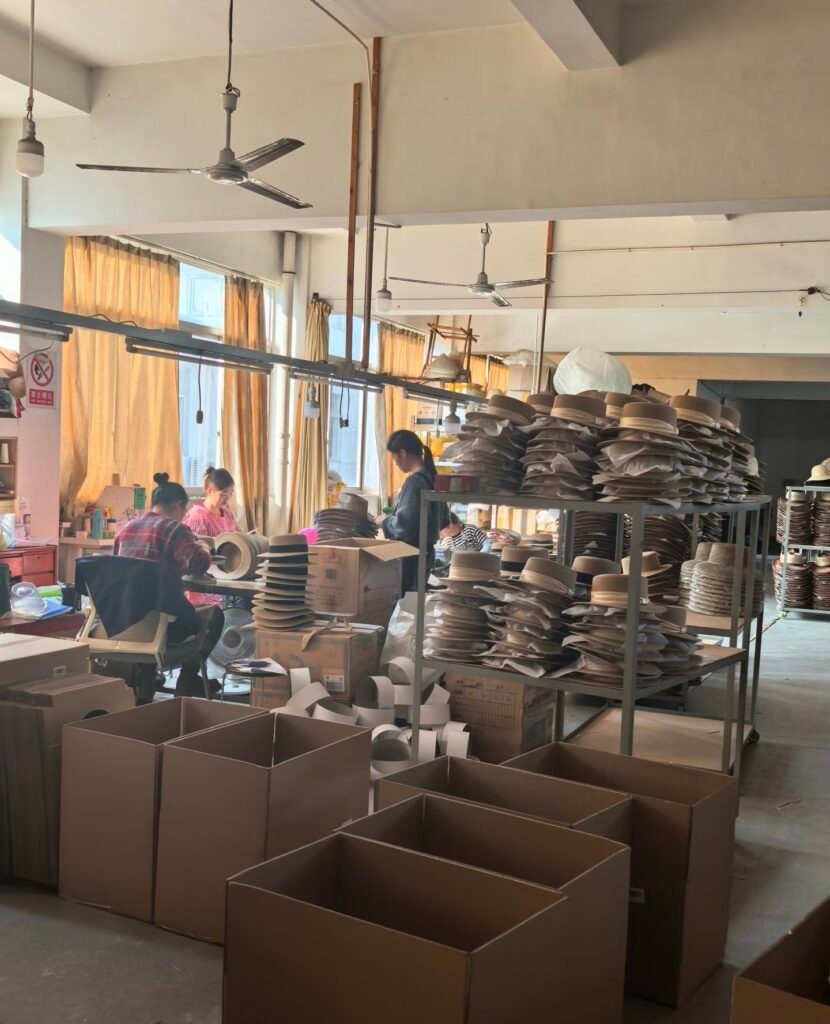 workshop where workers are assembling and packing straw hats, with hats placed on shelves ready for further processing or shipment.