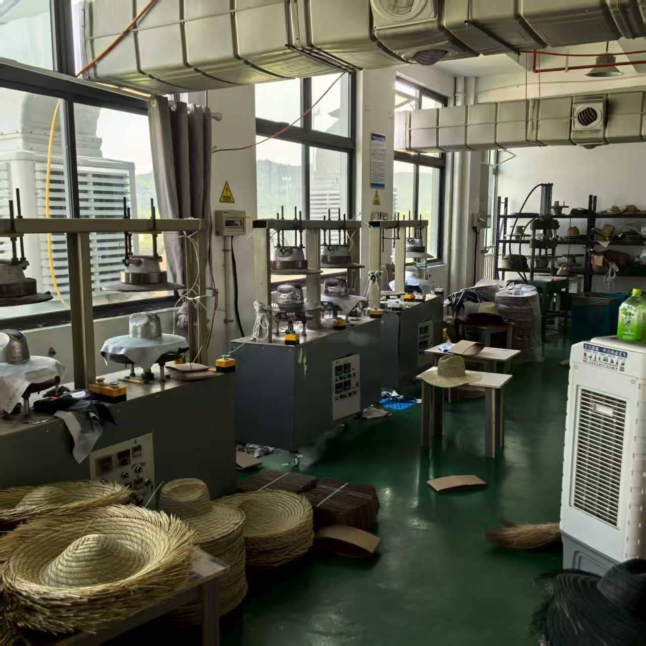 Straw hat shaping machines in operation at a wide brim beach hat manufacturing workshop.