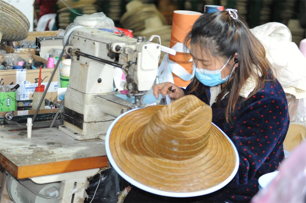 Worker stitching an OEM straw hat at a straw hat manufacturer factory