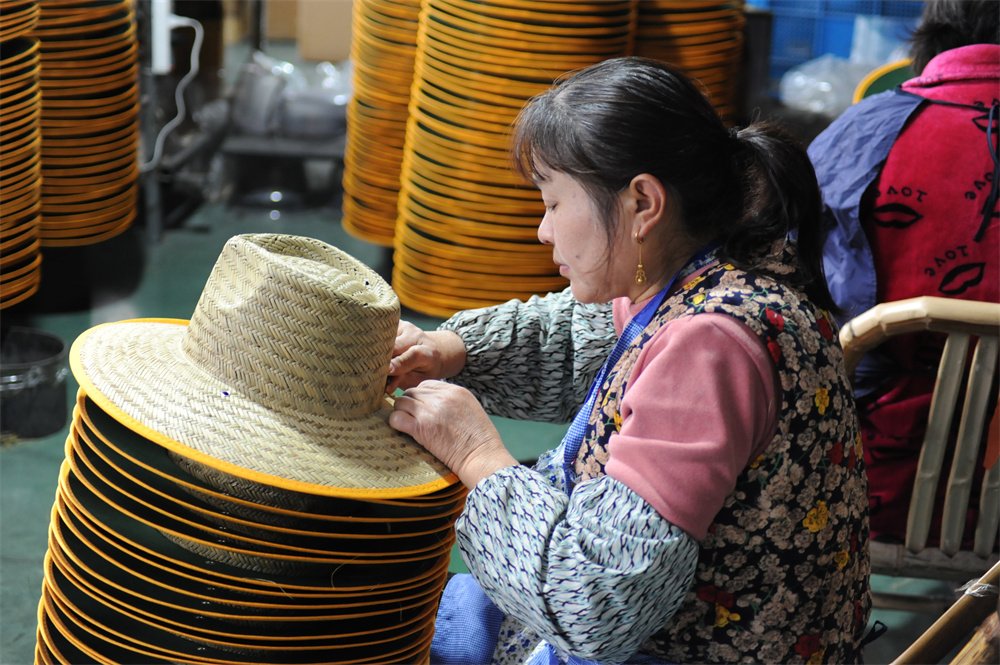 Factory worker trimming loose threads on straw hats during production