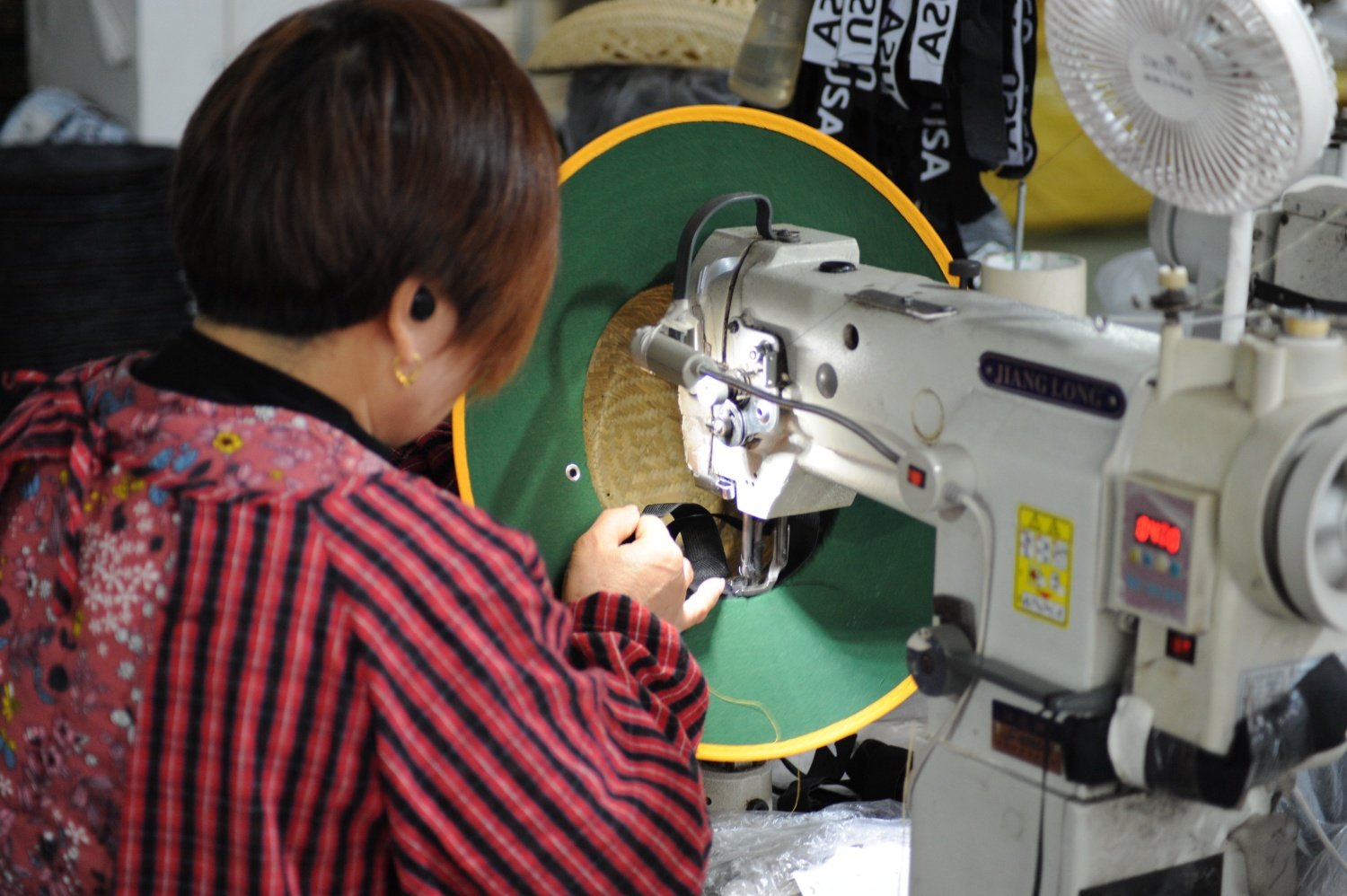 Worker sewing brim edge on straw hat using industrial stitching machine